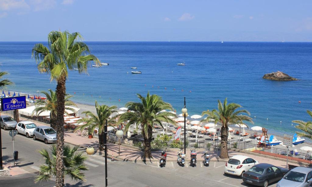 Pludmales ainava ar palmu kokiem un mierīgu jūru, kurā peld laivas. Redzama viesnīca "Elitotel" un sauļošanās vietas ar saulessargiem.