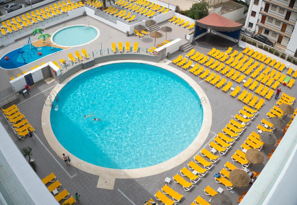 Peldbaseins ar skaidru zilo ūdeni un dzeltenām sauļošanās krēslām ap to, kā arī bērnu rotaļu baseins un palmām. Ideāla vieta atpūtai un izklaidei.