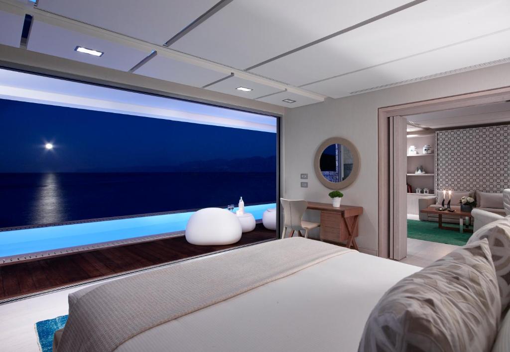 Mūsdienīgs guļamistabas interjers ar panorāmas logu, kas paver skatu uz jūru un mēnesi. Telpā ir stilīgi mēbeļu elementi un relaksējoša atmosfēra.