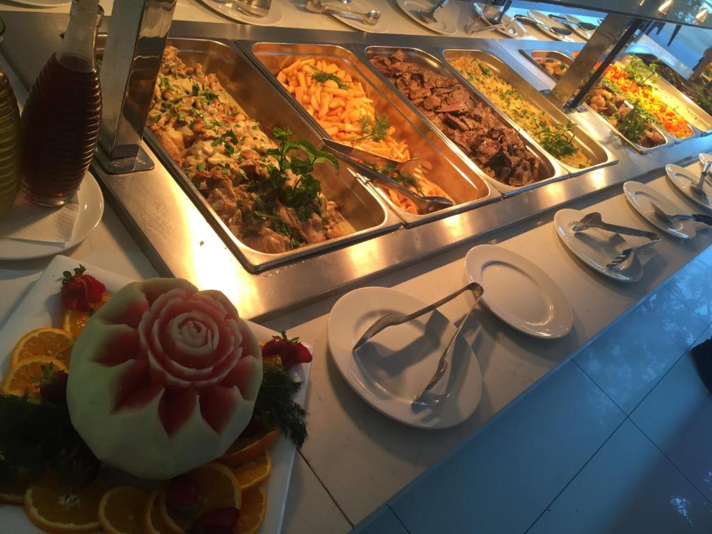 Bagātīga bufete ar dažādiem ēdieniem, tostarp gaļu un dārzeņiem, un dekoratīva arbūzu veidojuma rožu formā.