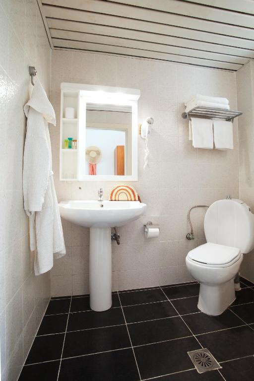 Mūsdienīgs un gaišs vannas istabas interjers ar melno grīdu, baltu izlietni un tualeti, kā arī spoguli un dvieļu plauktu.