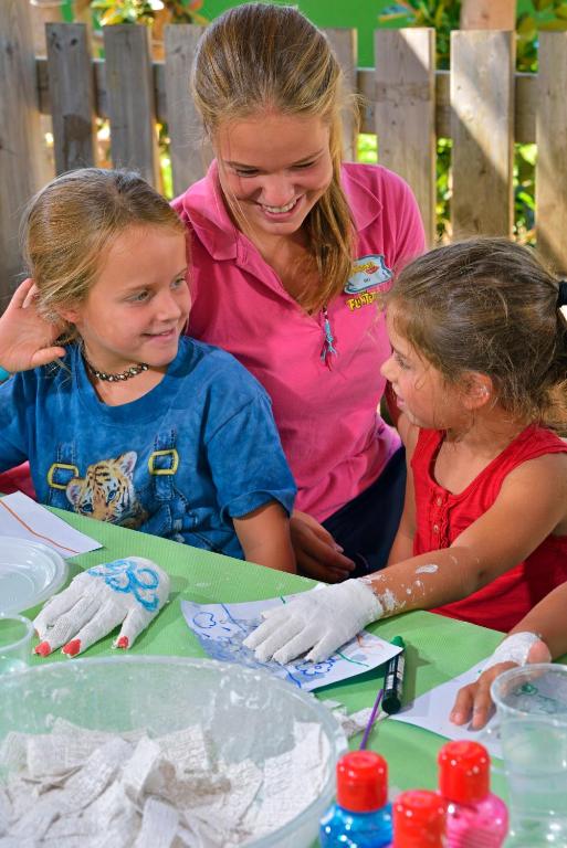 Bērni un pieaugušais kopā piedalās radošajā aktivitātē, zīmējot un mākslinieciski izklaidējoties. Gaisotne ir priecīga un draudzīga.