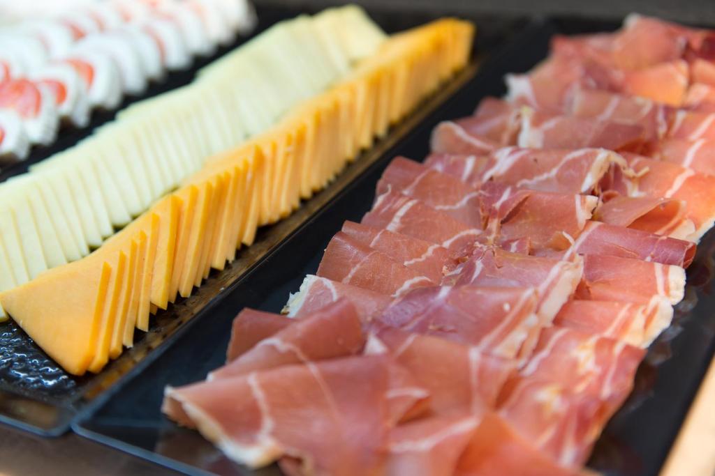 Dažādu siera un gaļas šķēļu izvēle, kas sakārtota uz melna šķīvja, radot vizuāli pievilcīgu uzkodu plati.