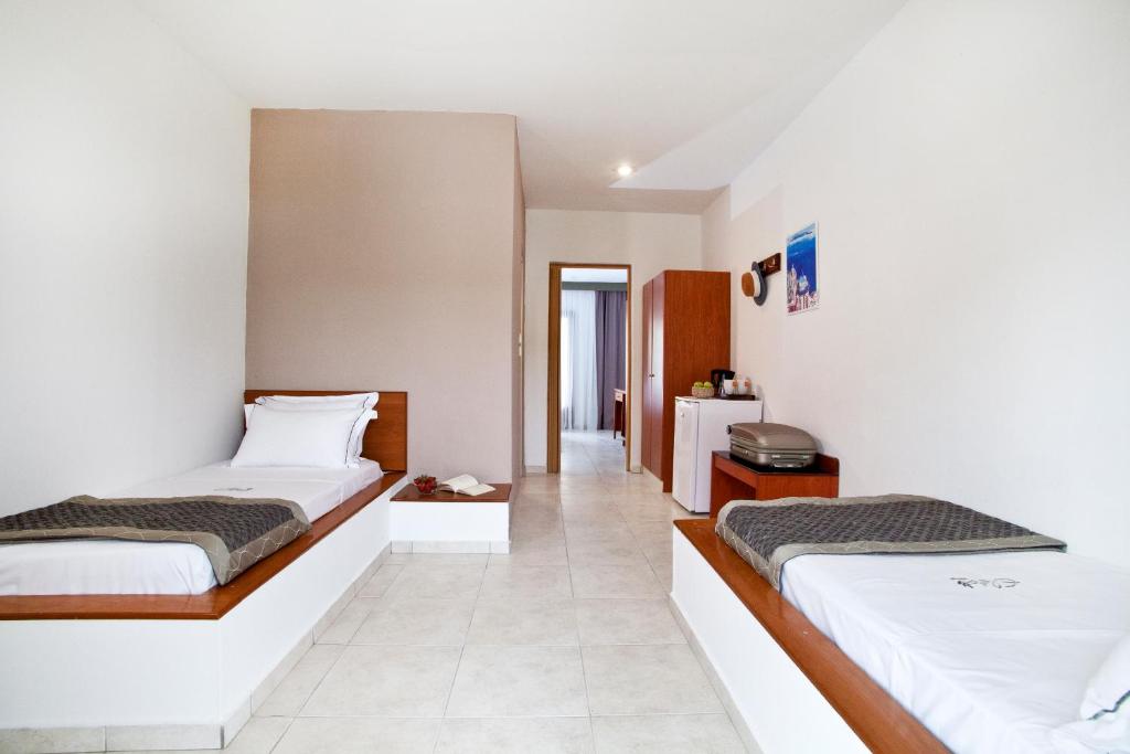 Gaiša un moderna viesnīcas istaba ar divām atsevišķām gultām, koka mēbelēm un nelielu ledusskapi. Telpā ir neitrālas krāsas un minimālistisks dizains, radot ērtu atmosfēru.