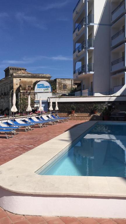 Baseina zona ar sauļošanās krēsliem un viesnīcu fona. Ēka ar balkoniem un skaidrām debesīm.