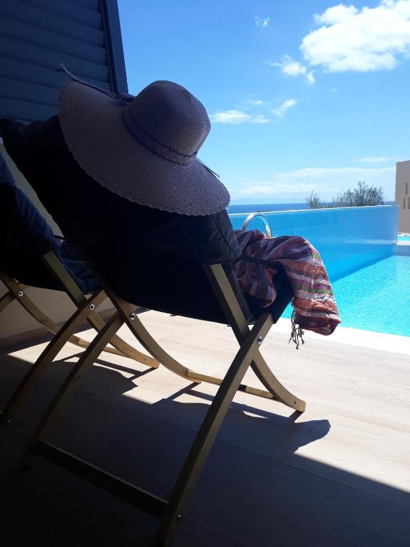 Sauļošanās krēsls ar platmalīti un šalli, blakus peldbaseinam, ar skatu uz zilo debesu fonu. Ideāla vieta relaksācijai un atpūtai.