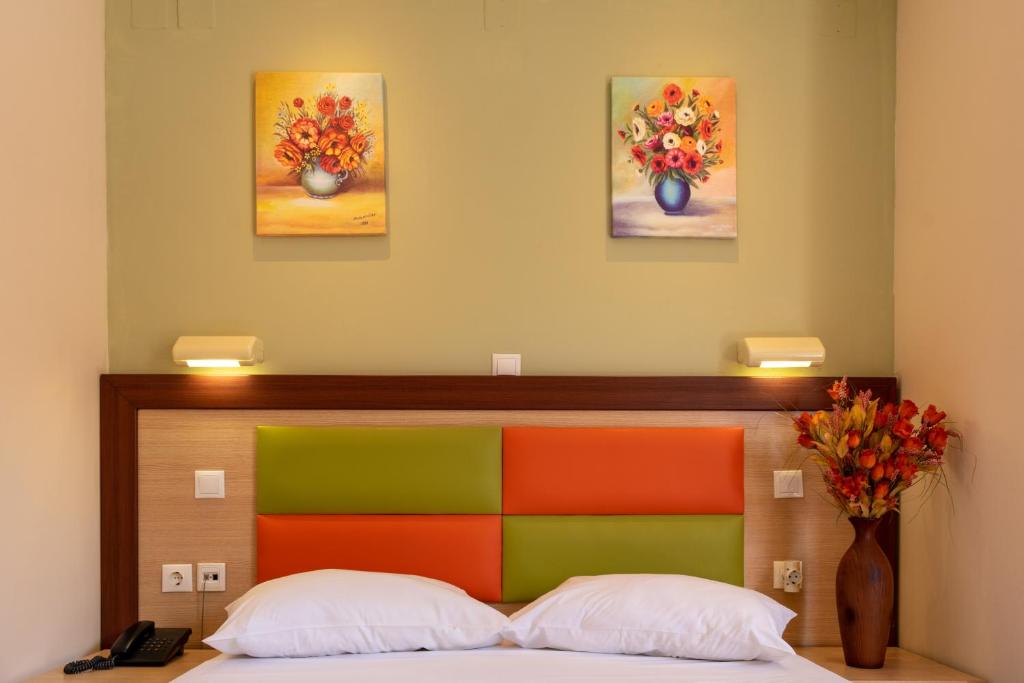 Gultas galvas apdare ar krāsainu dizainu, divas gleznas ar ziediem uz sienas un ziedu kompozīcija uz naktsgaldiņa.