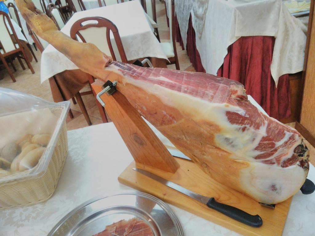 Sastāvdaļu statīvs ar šķiņķi, kas tiek pasniegts restorānā, blakus ir trauks ar maizēm un galdiņi ar galdautiem.