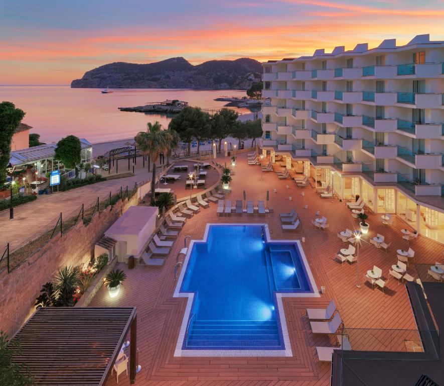 Mūsdienīgs viesnīcas komplekss ar peldbaseinu un terasi, kas atrodas pie jūras, ar skaistu saulrietu fonā. Apkārt ir zaļumi un ērtas atpūtas zonas.