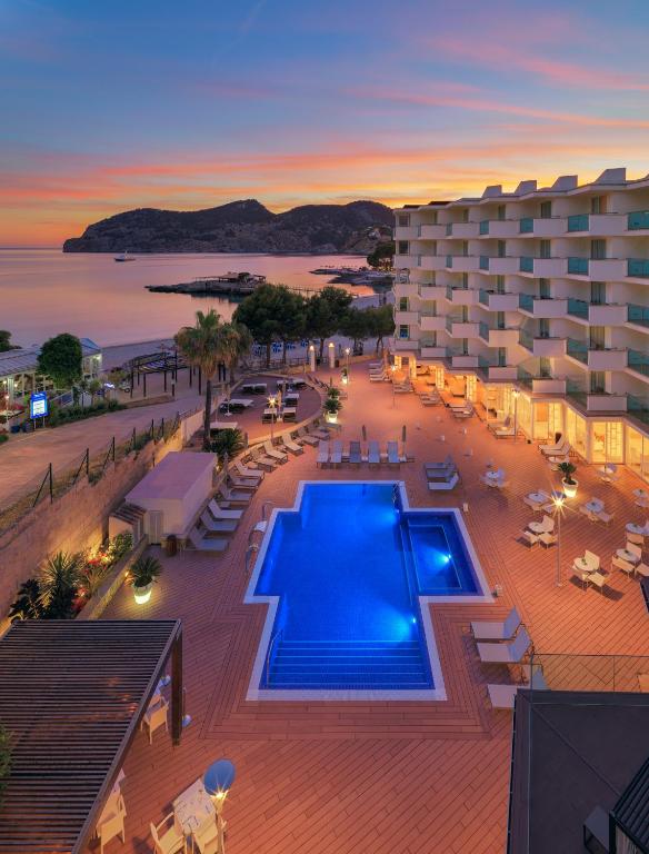 Viesnīcas baseins ar saulrieta skatu, apkārtne ar palmām un pludmali, kas atrodas netālu no kalniem.