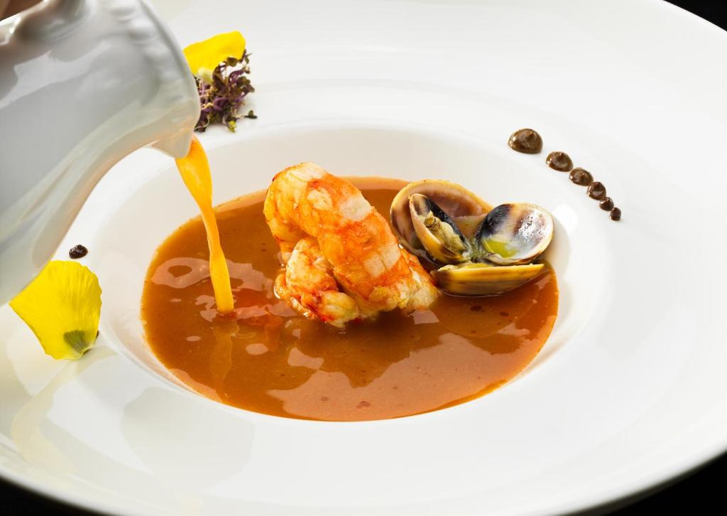 Garu zupa ar garnelēm un gliemenēm, dekorēta ar ziedlapiņām un mākslinieciskām detaļām.