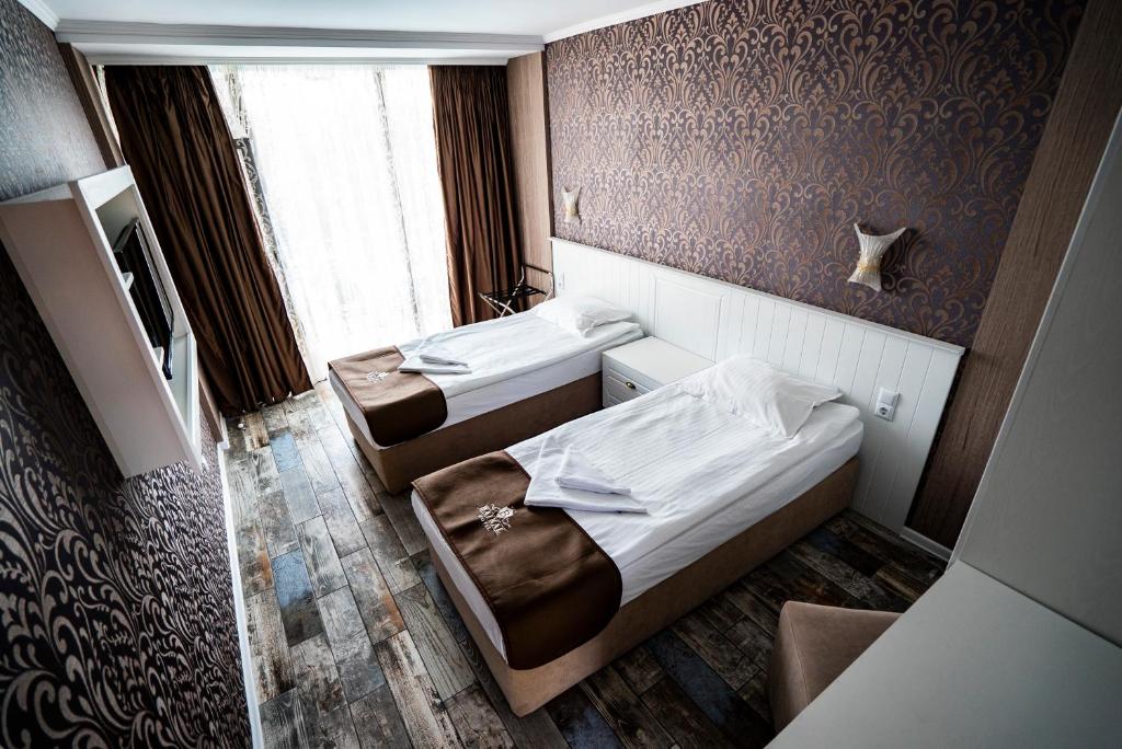 Mūsdienīgs viesnīcas numurs ar divām atsevišķām gultām un elegantu apdari, kas ietver brūnus un zeltainus akcentus. Labi apgaismots ar lieliem logiem un greznu tapetu.