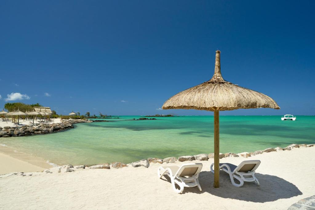 Pludmales ainava ar sauļošanās krēsliem un salmu jumtu, kas atrodas pie skaidra, zila ūdens. Fons veidojot mierīgu un relaksējošu atmosfēru.