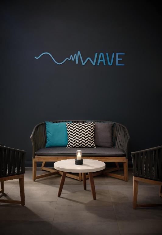 Mūsdienīga atpūtas zona ar tumšu sienu, kurā ir stilīgs dīvāns, spilveni un apaļa galdiņš ar sveci. Virs dīvāna ir uzraksts "WAVE".