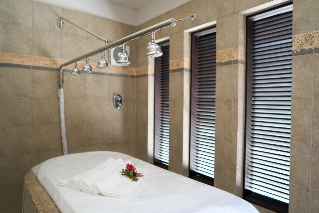 Spa telpa ar masāžas galdu, uz kura ir salocītas dvielīši un zieds, un ar modernām gaismām pie griestiem. Mierīga un relaksējoša atmosfēra.