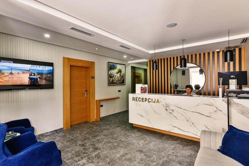 Mūsdienīga viesnīcas recepcija ar elegantu marmora letes dizainu, kurā redzama darbiniece, un televizors ar ainavām. Telpā ir moderna apgaismojuma sistēma un ērti sēdvietas.