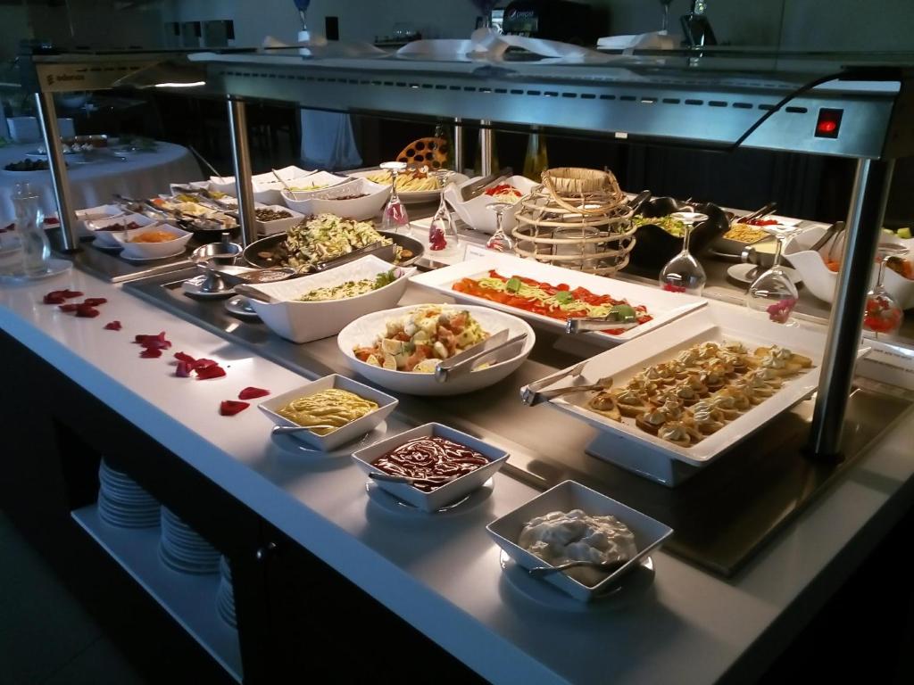 Bagātīgs bufetes galds ar dažādiem ēdieniem, tostarp salātiem, pastām un desertiem, dekorēts ar ziedlapiņām. Ideāli piemērots svinībām vai svētkiem.