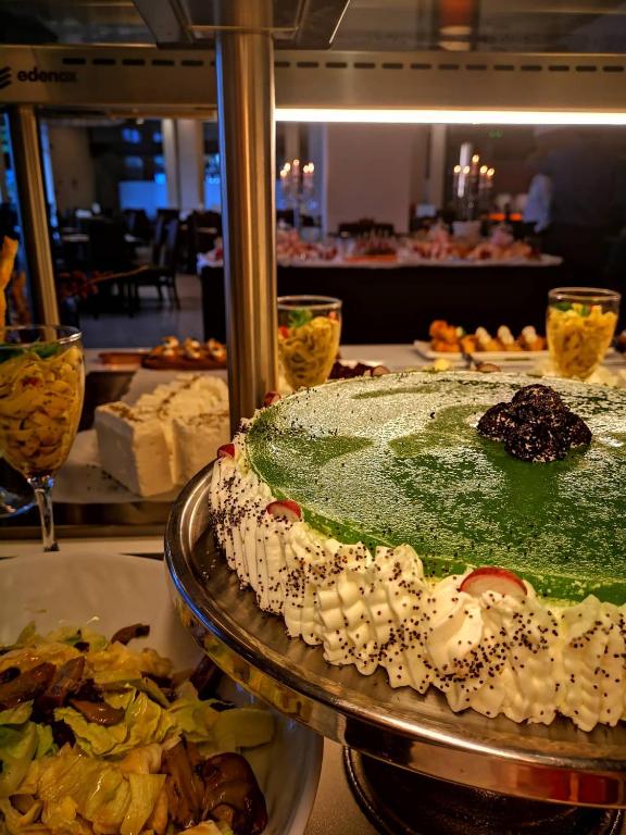 Zaļš deserts ar saldo krējumu un ogām, kas pasniegts viesību galda priekšplānā, fonā redzami citi ēdieni un sveces.