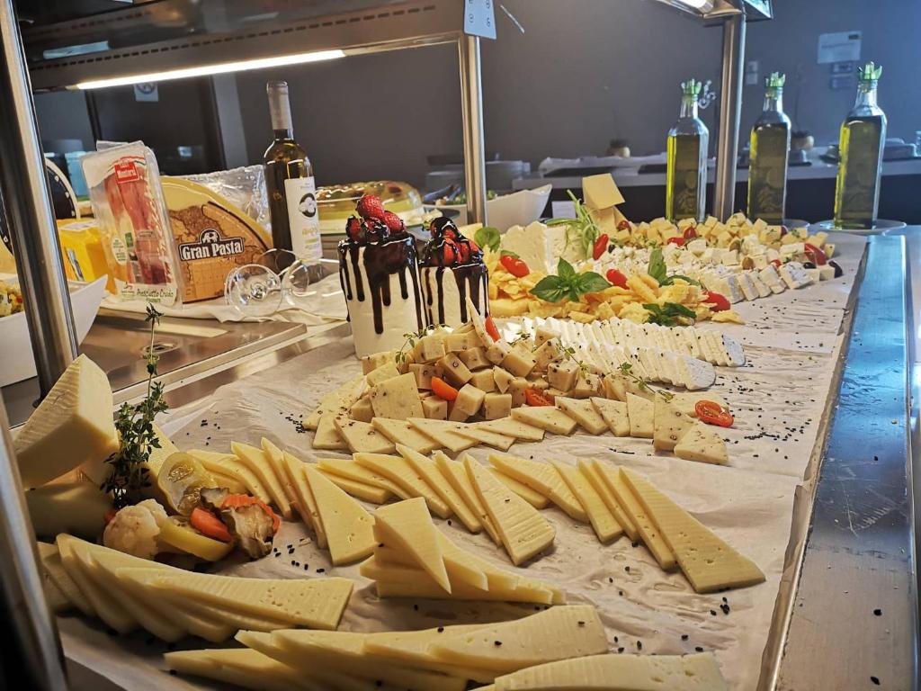 Siera un uzkodu bufete ar dažādām sieru šķirnēm, dārzeņiem un garšaugiem. Redzama arī olīveļļa un saldais deserts ar zemenēm.