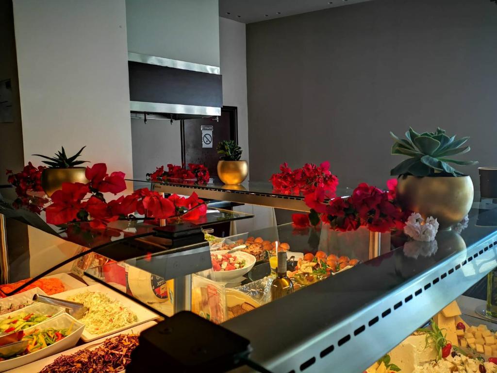 Buffet galda dekorācija ar ziediem un dažādiem ēdieniem, kas piedāvā krāsainu un pievilcīgu izvēli. Svaigi dārzeņi un salāti papildina ēdienu klāstu.