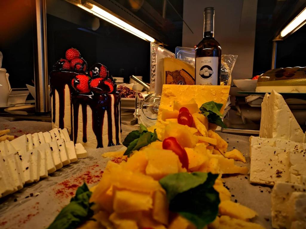 Siera galda izkārtojums ar dažādām siera šķirnēm, svaigiem dārzeņiem un saldējumu ar zemenēm un šokolādi. Fonā redzama pudele ar vīnu, kas papildina gardo ēdienu.