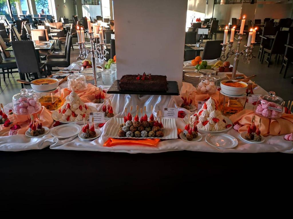 Deserta bufete ar dažādiem saldumiem, tostarp meringu, kūkām un šokolādes konfektēm, rotāta ar augļiem un sveču gaismu.
