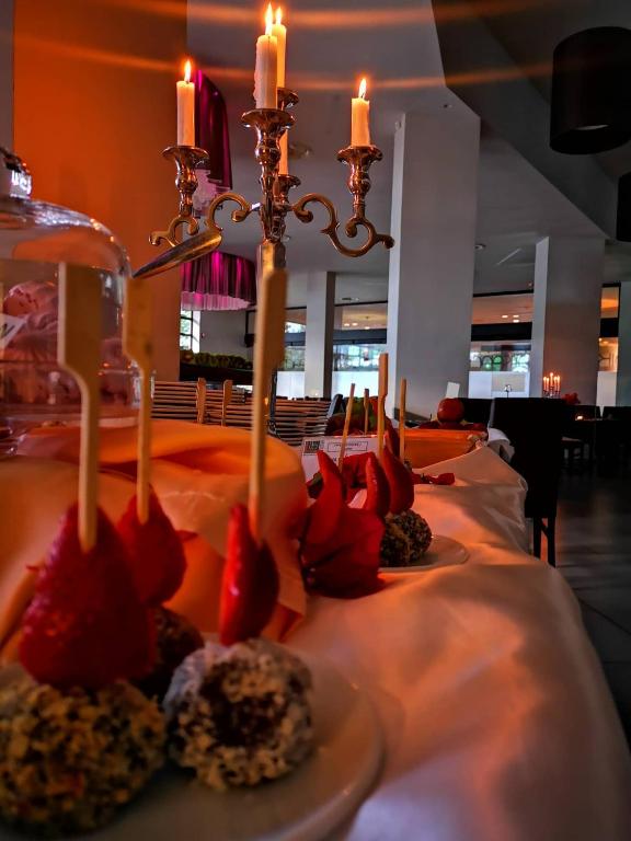 Elegants galda klājums ar svečturi un krāsainiem desertiem, tostarp zemenēm un šokolādes konfektēm, radot svinīgu atmosfēru.