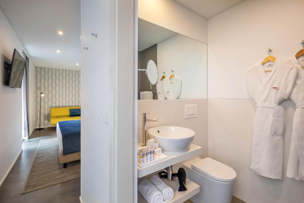 Mūsdienīgs viesnīcas numurs ar elegantu vannas istabu, kurā ir balti halāti un stilīgs izlietne. Numurā ir moderna televizora un dīvāna kombinācija, kas nodrošina komfortu un relaksāciju.