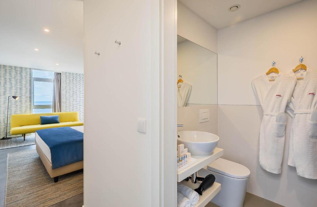 Mūsdienīgs viesnīcas numurs ar gaišām krāsām, dīvānu un vannas istabu, kas aprīkota ar dvieļiem un higiēnas precēm. Ideāls komfortam un relaksācijai.