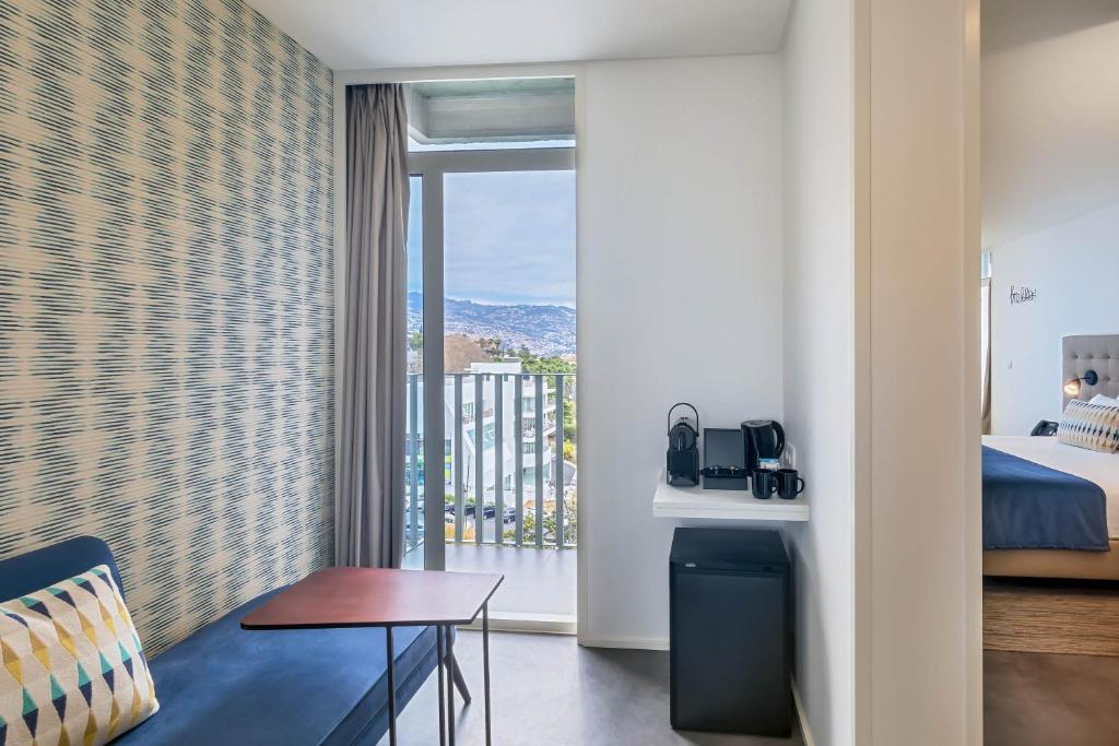 Mūsdienīgs viesnīcas numurs ar balkonu, kurā ir dīvāns un galdiņš, kā arī kafijas automāts un mini ledusskapis. No loga paveras skats uz ainavu.