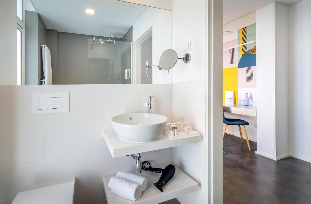 Moderns vannas istabas interjers ar elegantu izlietni, spoguli un matu žāvētāju, kas redzams uz plaukta. Fona sienā ir gaiša krāsa un mūsdienīgs dizains.