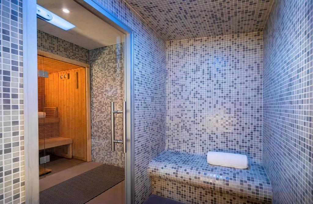 Mūsdienīga sauna ar mozaīkas flīzēm un koka elementiem, kas nodrošina relaksējošu atmosfēru. Telpa ir aprīkota ar sēdvietām un dvieli, radot ideālu vidi atpūtai.