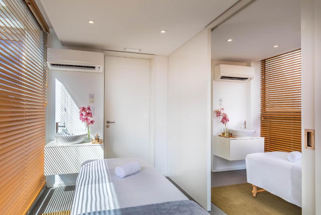 Mūsdienīga un gaiša relaksācijas telpa ar divām masāžas gultām, dekorēta ar rozā orhidejām un koka žalūzijām, kas nodrošina dabīgu apgaismojumu.