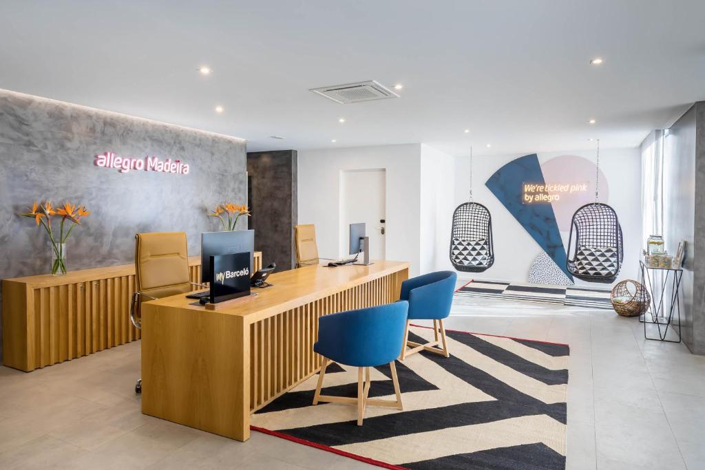 Moderns viesnīcas reģistratūras interjers ar koka mēbelēm, zilu krēslu un stilīgu dekoru. Gaismas elementi rada viesmīlīgu atmosfēru.