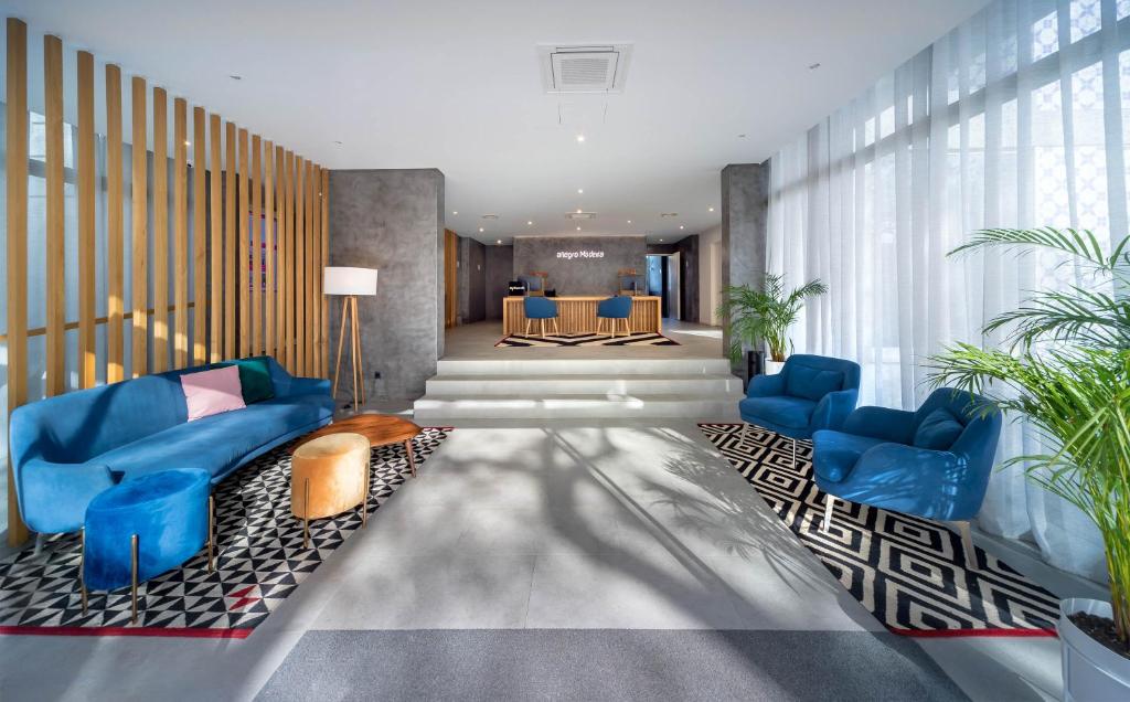 Mūsdienīgs viesnīcas vestibilis ar spilgtiem dīvāniem, krēsliem un stilīgu grīdas paklāju, radot siltu un viesmīlīgu atmosfēru. Gaismas un augu elementi piešķir telpai dzīvīgumu.