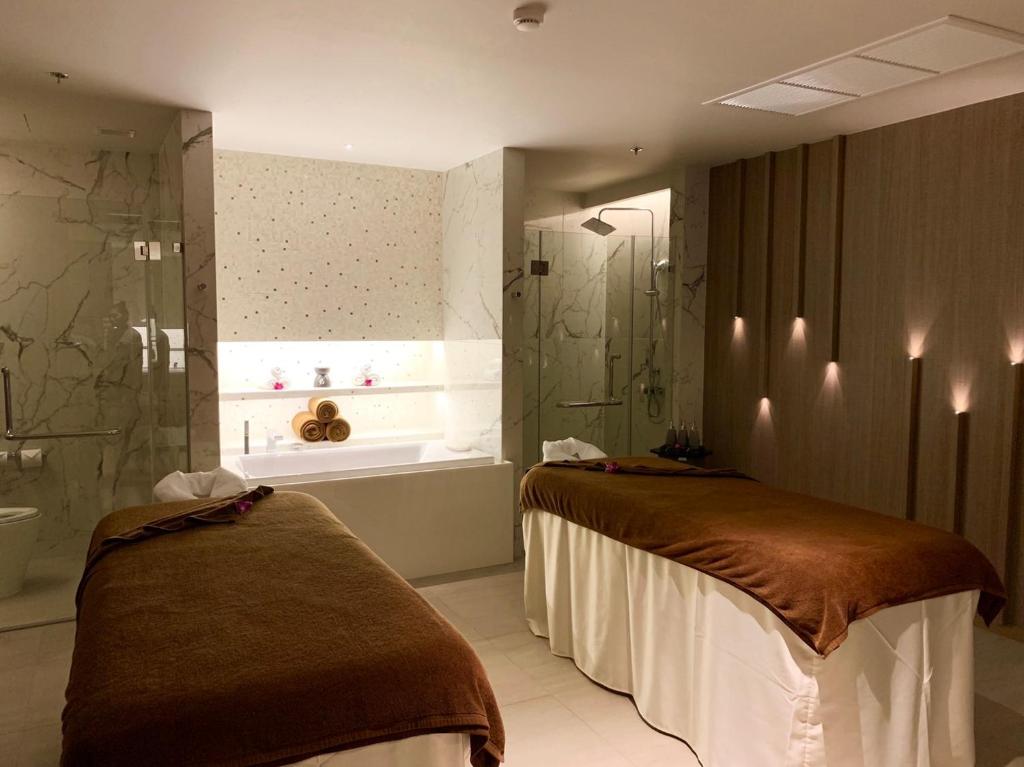 Mūsdienīgs spa telpas interjers ar divām masāžas galdiem, relaksējošu atmosfēru un vannu, kas apgaismota ar mīkstu gaismu. Šī vieta ir ideāli piemērota atpūtai un atjaunošanai.