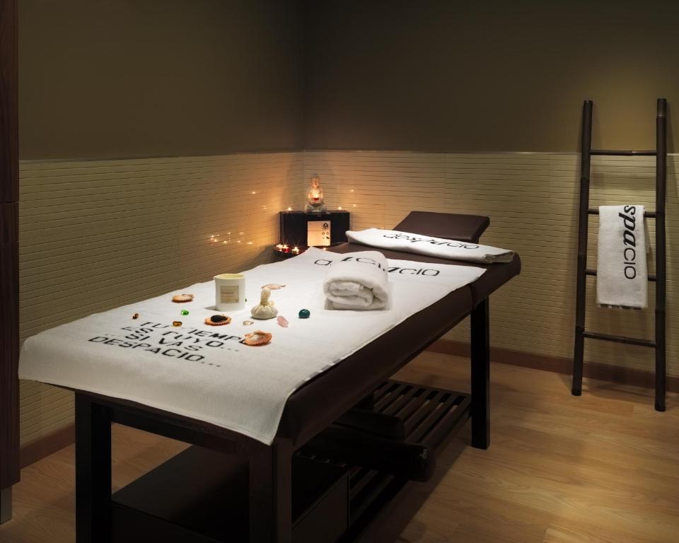 Relaksējoša masāžas telpa ar masāžas galdu, dekorētu ar dvieļiem un aromātiskām svečēm, radot mierīgu atmosfēru. Interjers ir vienkāršs un elegants, veicinot atpūtu un relaksāciju.