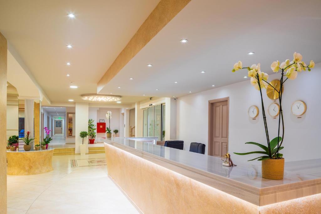 Mūsdienīgs viesnīcas reģistratūras interjers ar elegantiem elementiem, iekļaujot orhideju pušķi un minimālistisku dizainu. Gaisma rada siltu un viesmīlīgu atmosfēru.