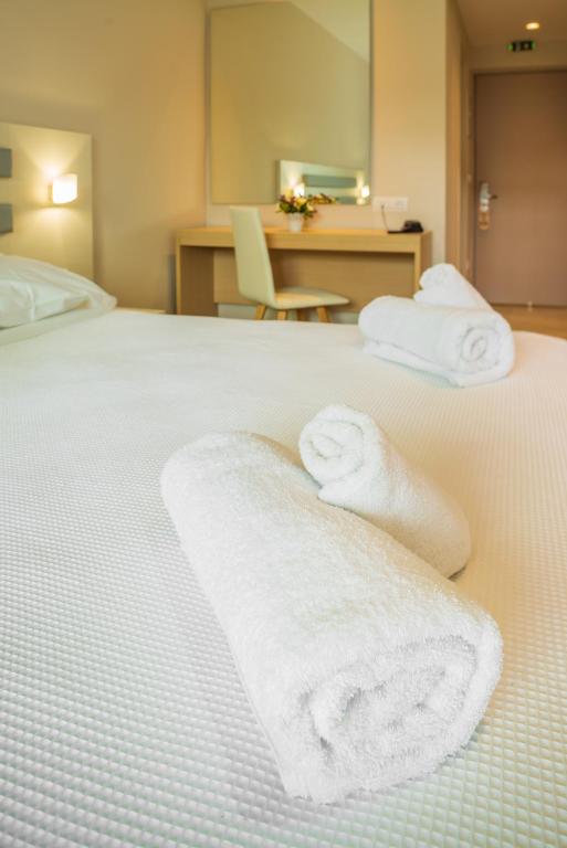 Mūsdienīgs viesnīcas numurs ar baltām dvielīšiem un gultu, kas ir kārtīgi sakārtota, radot mierīgu un relaksējošu atmosfēru. Spogulis un rakstāmpulciņš papildina interjeru.