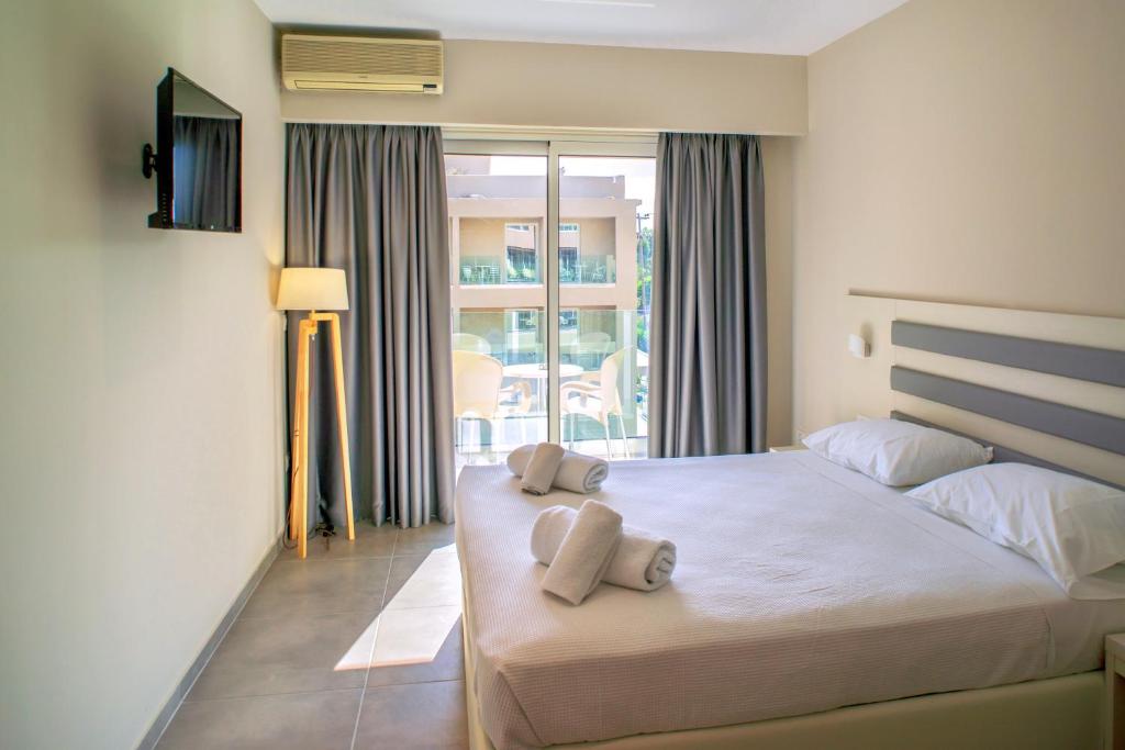 Mūsdienīga guļamistaba ar gultu, televizoru un lampu, kurā ir lieli logi ar skatu uz terasi. Telpa ir gaiša un eleganta, radot relaksējošu atmosfēru.