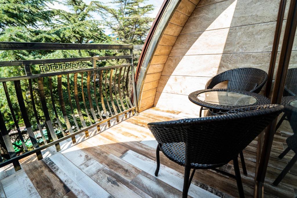 Balkons ar melnām vītņu krēsliem un stikla galdiņu, ap kuru redzama zaļa daba. Daba un mūsdienīgs dizains rada relaksējošu atmosfēru.