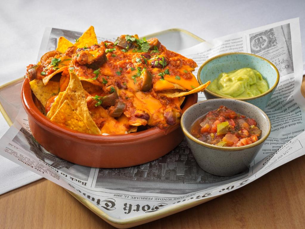 Svaigi cepti nacho čipsi ar siera mērci, gaļu un jalapeño, pasniegti ar salsa un guacamole blakus.