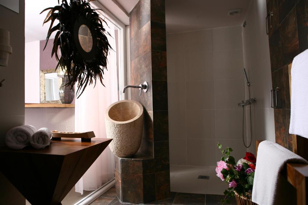 Mūsdienīgs vannas istabas interjers ar akmens izlietni, dušu un elegantu spoguli. Interjers papildināts ar ziediem un dvieļiem, radot relaksējošu atmosfēru.