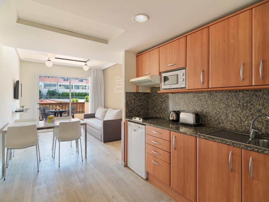 Mūsdienīga virtuve ar koka skapjiem un granīta virsmām, kas savienota ar ēdamzonu un viesistabu, kas ved uz āra terasi. Gaismas elementi un plašas logi rada gaišu un viesmīlīgu atmosfēru.