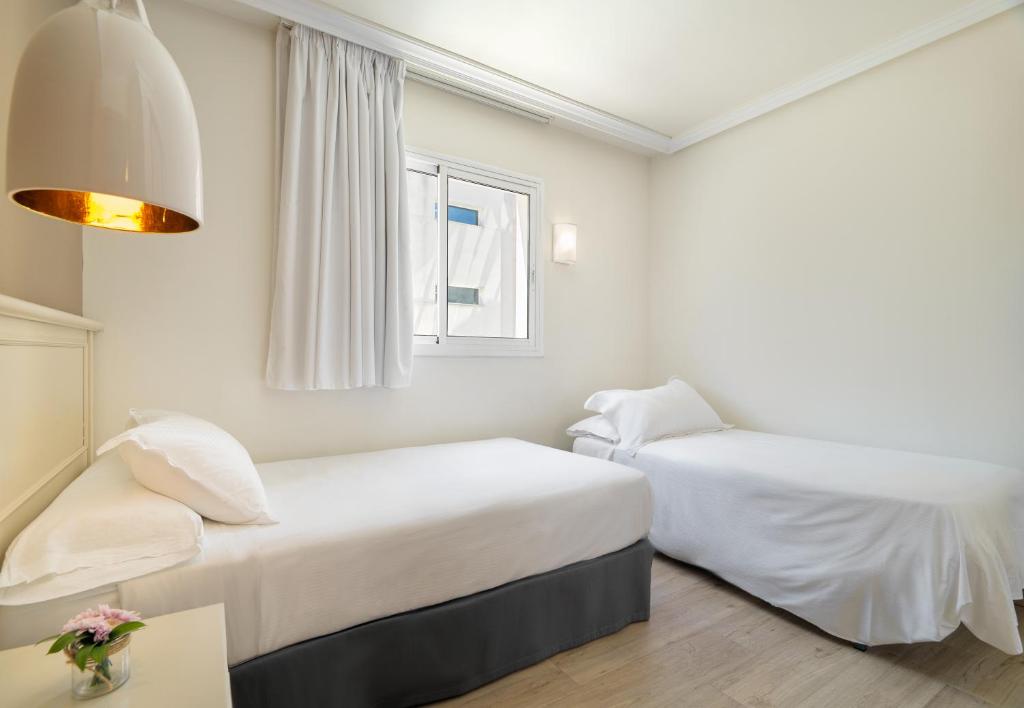 Mūsdienīga guļamistaba ar divām atsevišķām gultām, gaišām krāsām un logu, kas nodrošina dabisko apgaismojumu. Galda rotājums ar ziediem pie gultas pievieno mājīgumu.