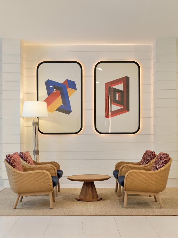 Mūsdienīgs viesnīcas interjers ar divām ģeometriskām gleznām uz sienas un ērtām vīnogu krāsas krēsliem, kas apņem apaļo galdu.