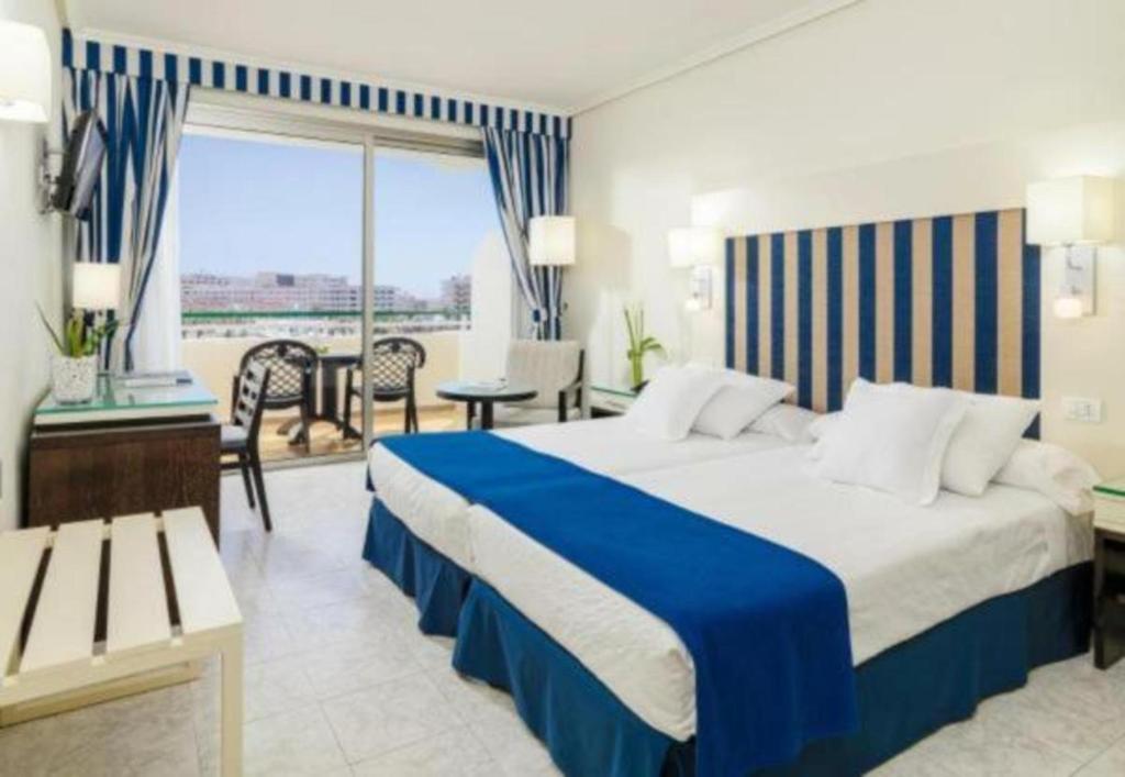 Mūsdienīgs viesnīcas numurs ar divām gultām, zilām akcentu krāsām un viesistabu, no kuras paveras skats uz āru. Numurā ir televizors, galda vieta un balkons.