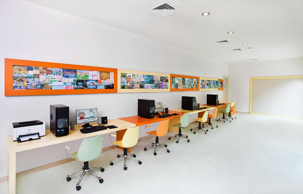 Mūsdienīgs datora kabinets ar vairākām darba vietām, kur katrā ir dators un krēsls. Sienas rotā krāsaini mākslas darbi, kas piešķir telpai radošu atmosfēru.