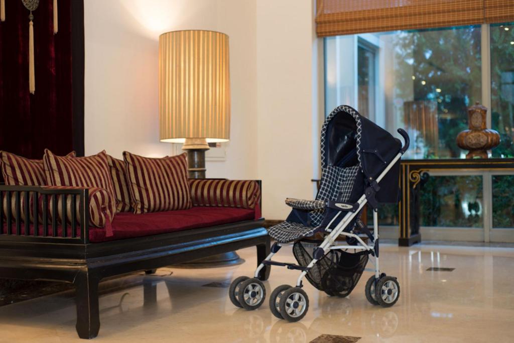 Bērnu ratiņi stāv eleganti iekārtotā telpā ar mīkstiem dīvāniem un apgaismojumu. Interjers izceļas ar greznu dizainu un siltām krāsām.