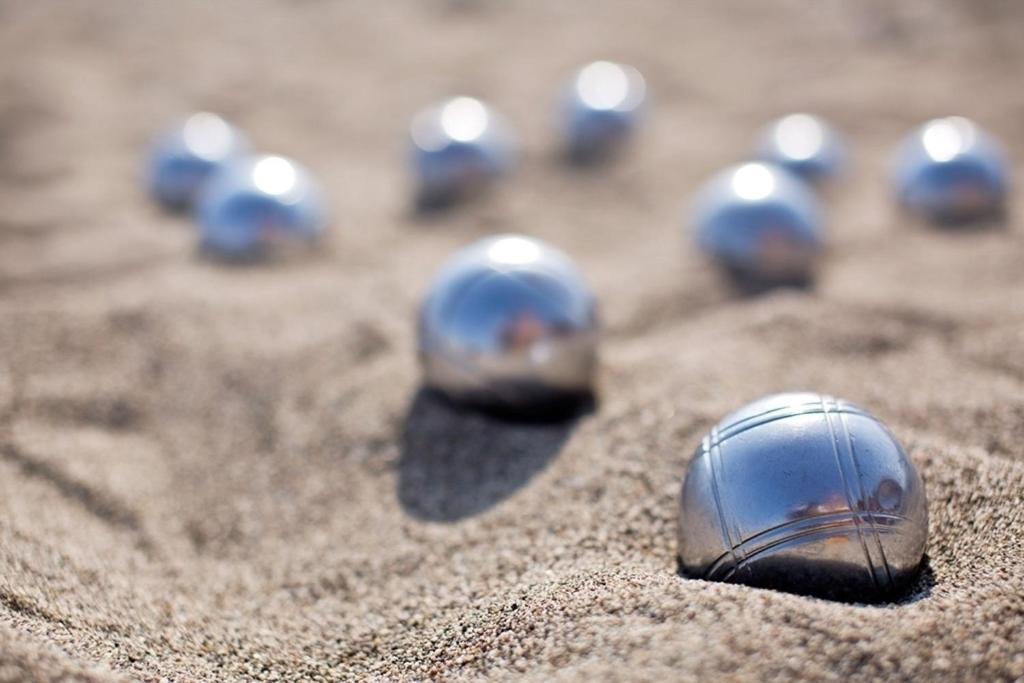 Metāla bumbiņas smiltīs, kas izmantojas petankā. Bumbiņas ir spožas un atspoguļo saules gaismu, radot pievilcīgu ainavu.